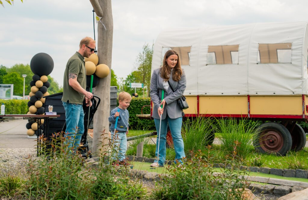 Volwassenen en een kind met golfclubs bij een minigolfbaan